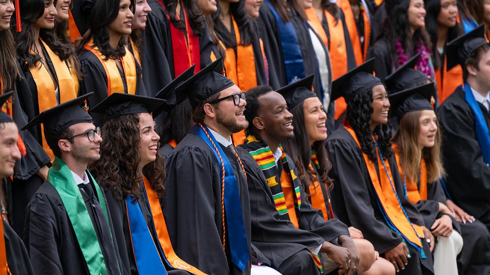 A group of smiling students wearing graduation robes and caps with many different colored sashes