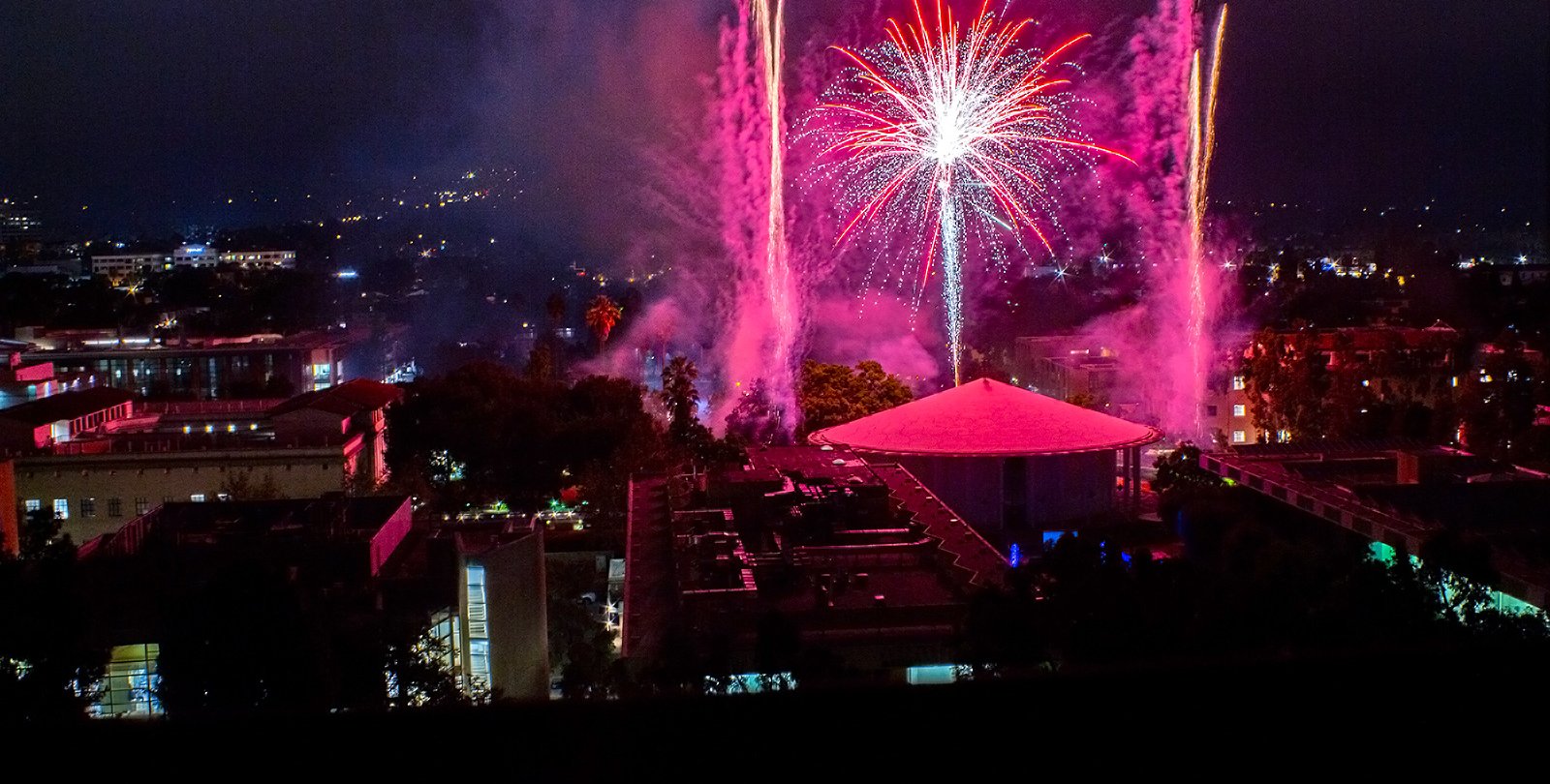 Red and pink fireworks light up the night sky over Beckman Auditorium