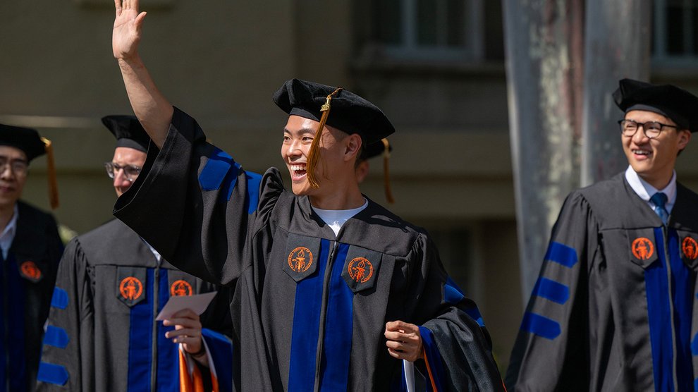 Three Caltech graduates enter their commencement ceremony. One is waving to someone outside the photo's frame.