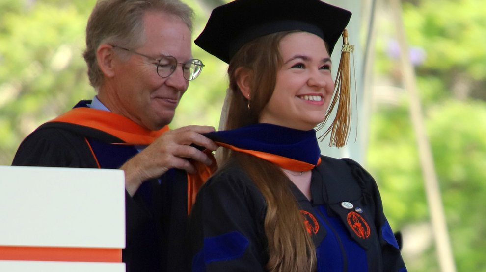 An older man wearing glasses places an orange stole around the neck of a woman who is graduating from Caltech