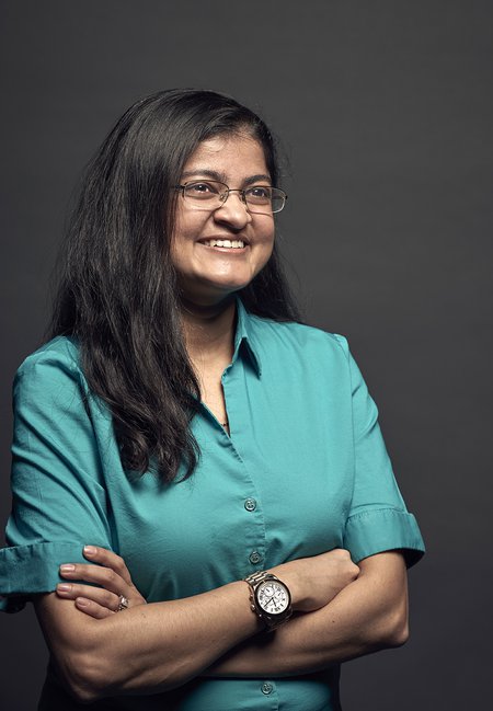 Mansi Kasliwal smiles with her arms crossed. She wears a button-down shirt in front of a black backdrop.
