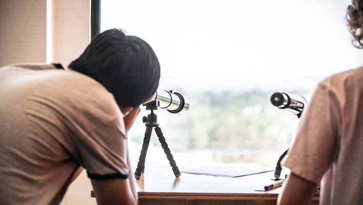 student looking into the sky through a telescope