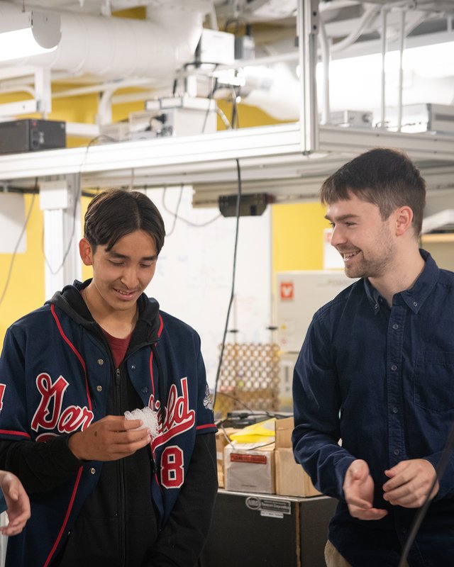 In a laboratory setting, two people smile as one looks at a cube of porous material in his hand