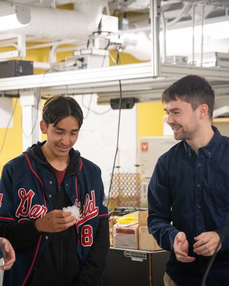 In a laboratory setting, two people smile as one looks at a cube of porous material in his hand