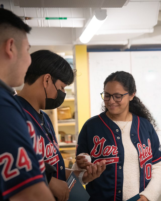 Three people stand in a brightly lit laboratory, one handing a ball of white material to another