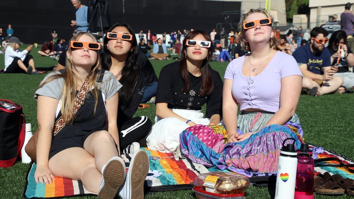 Four teenage girls wearing eclipse glasses on athletic field