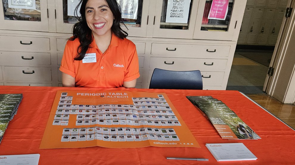 Jaclyn Kietzman smiles behind an orange-draped table containing brochures about Caltech