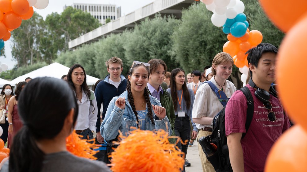 Among a group of students entering Beckman Auditorium, one student cheers while smiling at the camera.