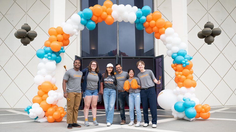 A group of Caltech staff pose in front of a balloon arch in front of Beckman Auditorium