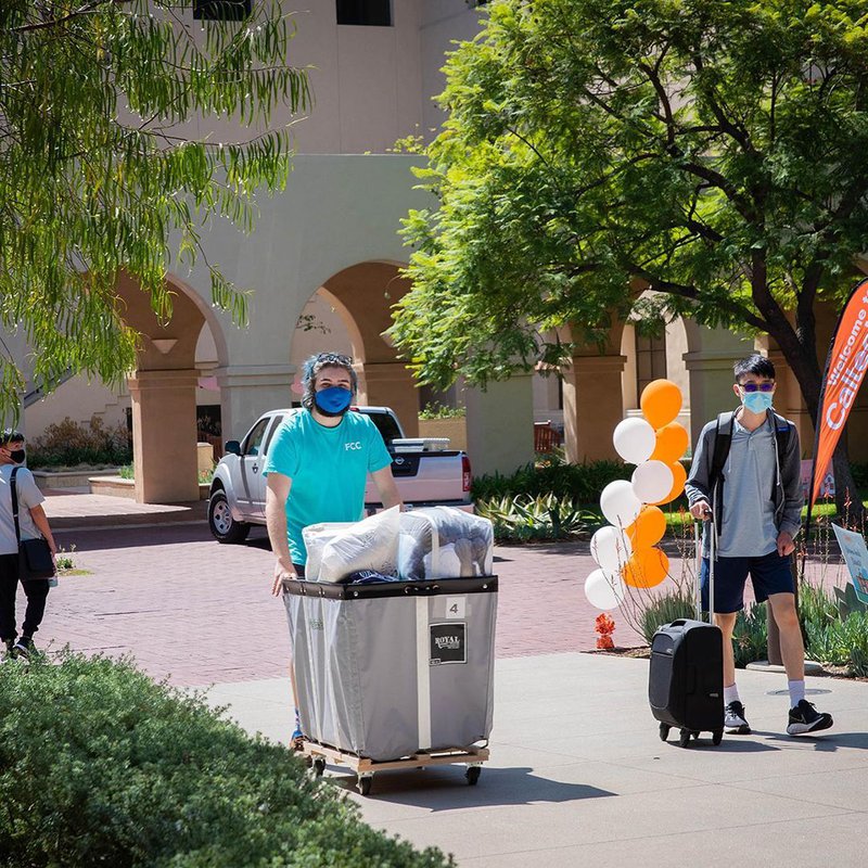 A student pushes a cart full of her belongings through campus.