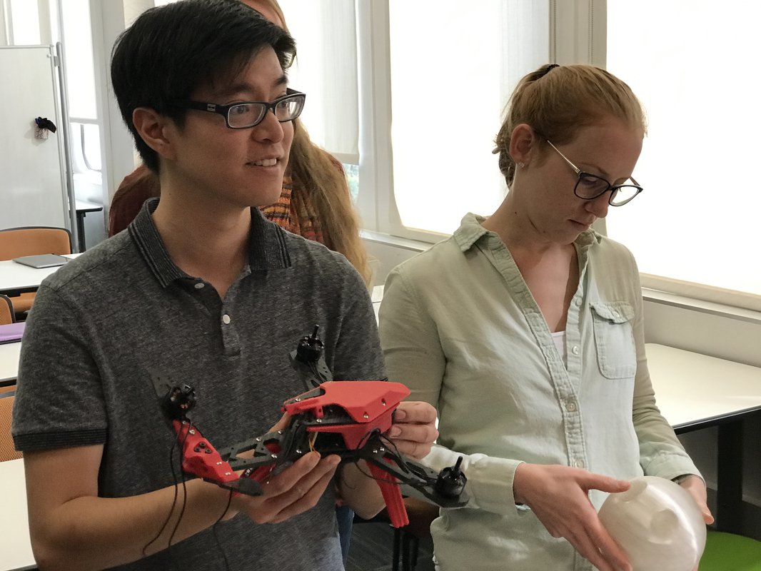 Students examine a 3D printed drone and a round component designed to hold a stylized table's legs in place.