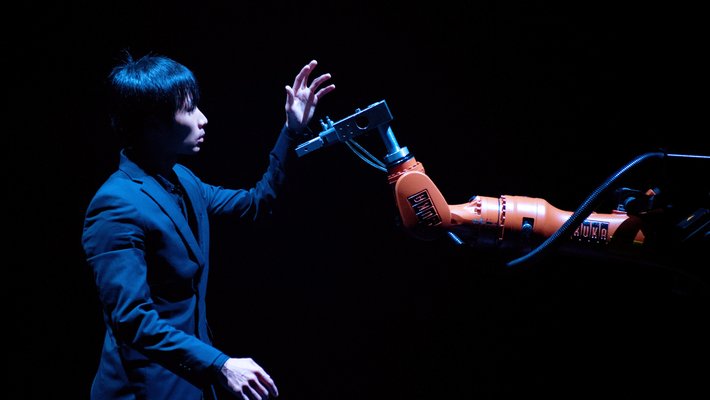 darkly lit scene, person in a suit holding up a hand to a robot hand