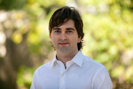Portrait of Nicholas Adams-Cohen in a white collared shirt on a green, out of focus background