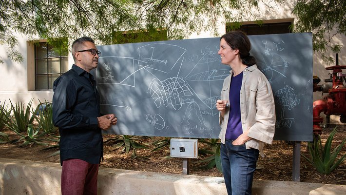 two people in discussion in front of an outdoor chalkboard