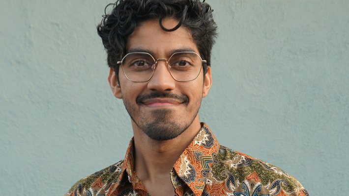 A person with dark hair and glasses smiles for a photo