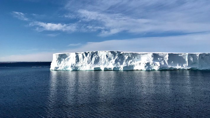 Blue ocean with a white iceberg in the distance and a bright blue sky