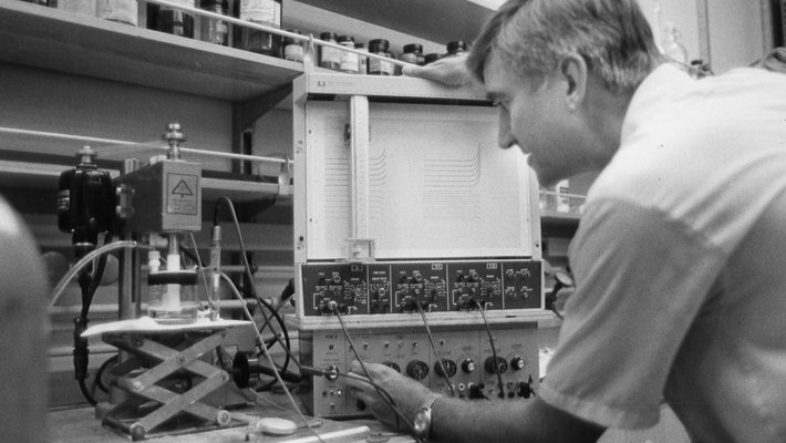 A man seen from behind, adjusting scientific equipment in a chemistry lab.