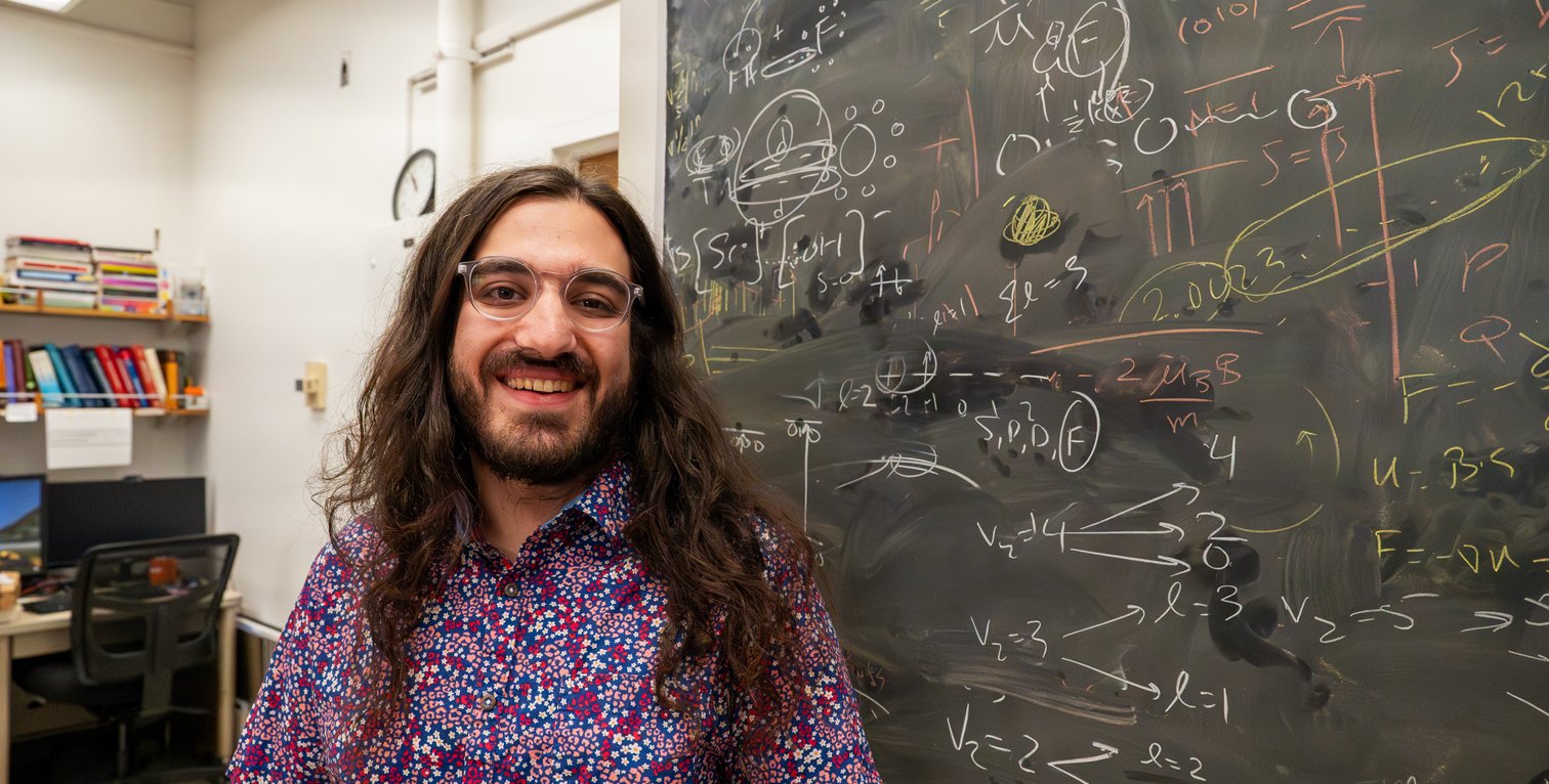 Student standing in front of a chalkboard with many equations