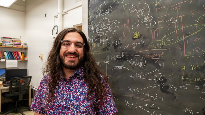 Student standing in front of a chalkboard with many equations