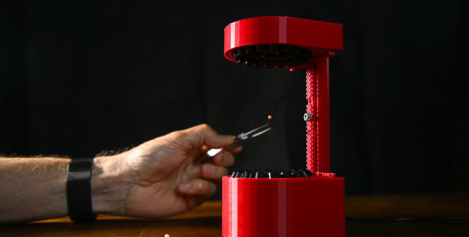 A hand places a pellet into a 3D-printed ultrasonic levitator.