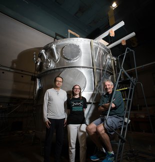 Members of the nEDM team stand in front of their magnetic cryovessel experimental apparatus