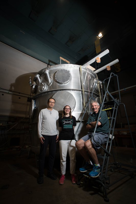 Members of the nEDM team stand in front of their magnetic cryovessel experimental apparatus