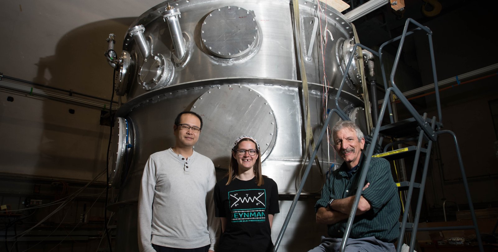 Members of the nEDM team stand in front of their magnetic cryovessel experimental apparatus