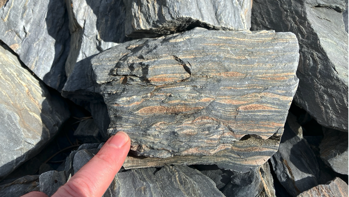 A person's finger points to stripes on a rock