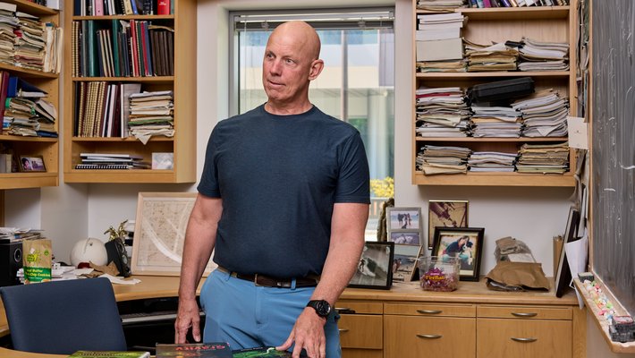 Image of Rob Philiips leaning against a desk with shelves of books behind him