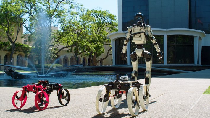 a humanoid robot and two rolling robots in front of Caltech Hall and its fountain at Caltech