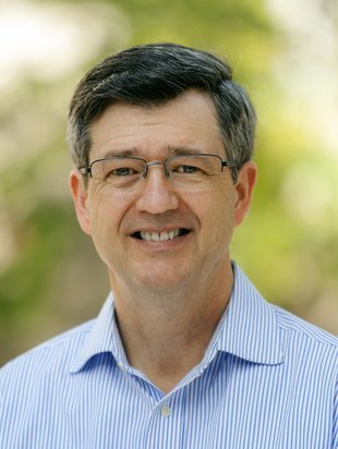 A portrait of Warren Brown. He is outdoors and wears glasses and button-up shirt.