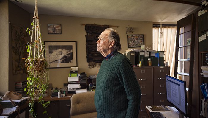 Ted Scudder, professor emeritus of anthropology, stands in his office. He is surrounded by file folders, books, and artifacts.