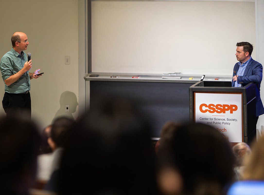 Person holding microphone asking a question to person standing at podium