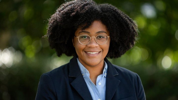 A portrait of Danielle Wiggins. She is outdoors and wears a blazer and button-down shirt.