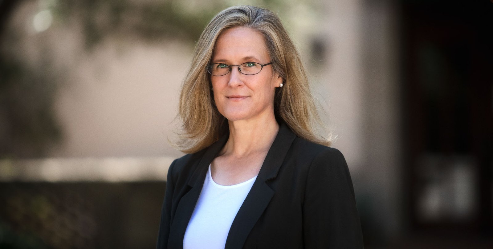 A portrait of Tracy Dennison. She is outside and wears a blazer.