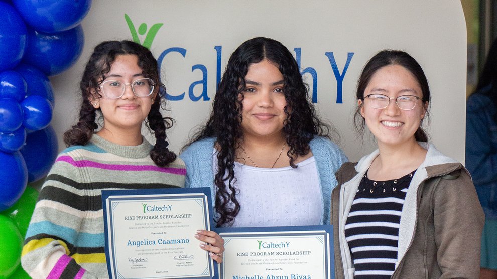 Three people stand, smiling, in front of a display with the words "Caltech Y"