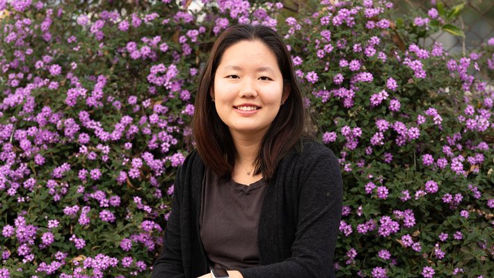 Yiyi Cai is pictured sitting against a background of purple flowers.