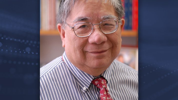 Sunney Chan smiles at the camera without showing his teeth. He wears glasses, a blue and white striped shirt, and a red tie with a print of horses jumping over a gate.