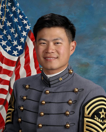 A young man in a military uniform with the American flag behind him.