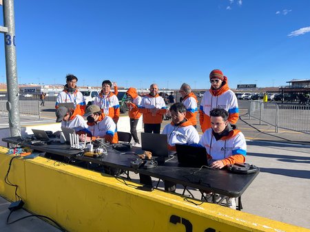 Caltech Racer team members wearing orange and white jackets, working on laptops to prepare the autonomous race car for its time trial