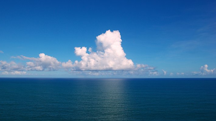A photo of clouds lingering over an expanse of ocean.