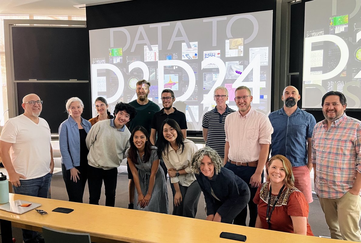 14 people standing and smiling behind a table with screens behind them