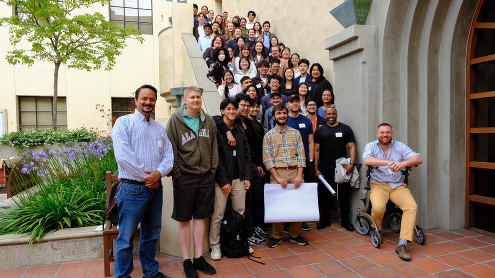 Mentors, mentees, and organizers arranged along a set of stairs outside. One man is sitting in a wheel chair in the lower right corner.