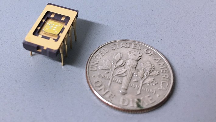 A small integrated circuit rests on a surface next to a time, which is comparable in size