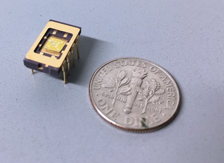 A small integrated circuit rests on a surface next to a time, which is comparable in size