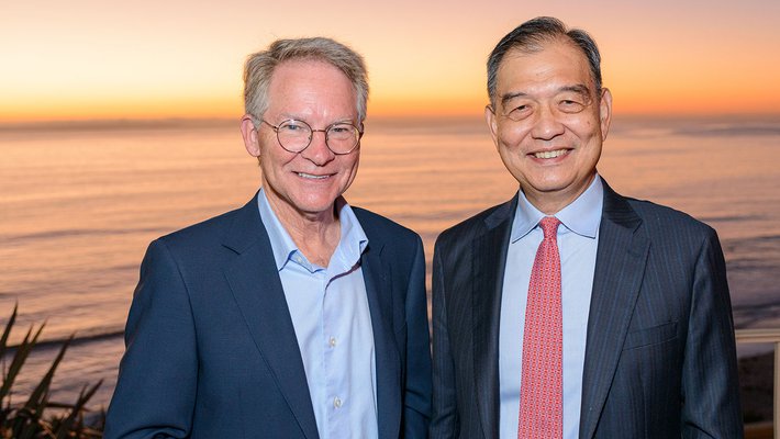 Cropped photo of two men in suits standing before a sunset
