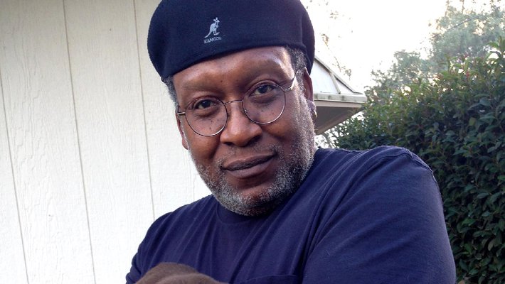 Don Crewell, former director of financial aid, holds a chocolate lab puppy and looks into the camera. He wears a beret.