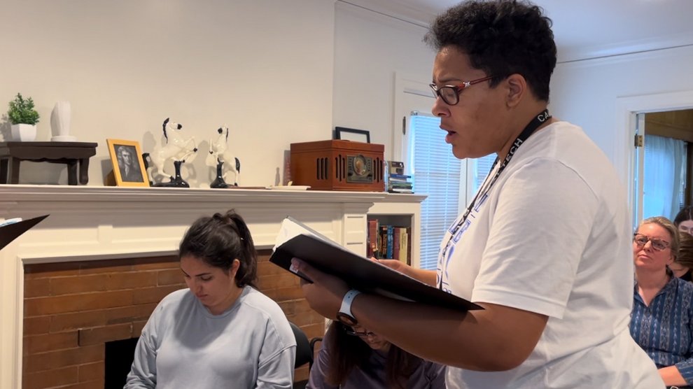 A person holding a music folder and singing in a room in a house