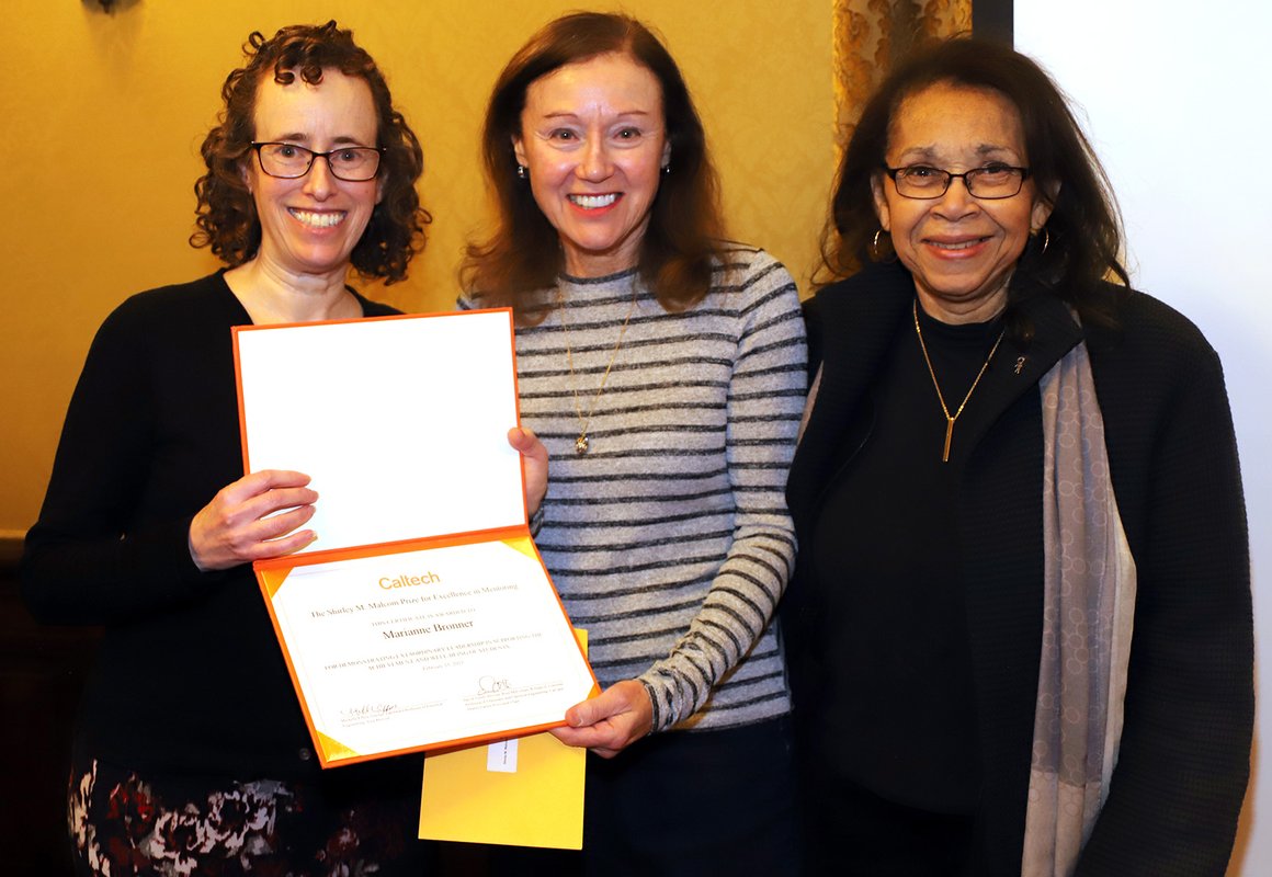 Three women pose for a photo with an award