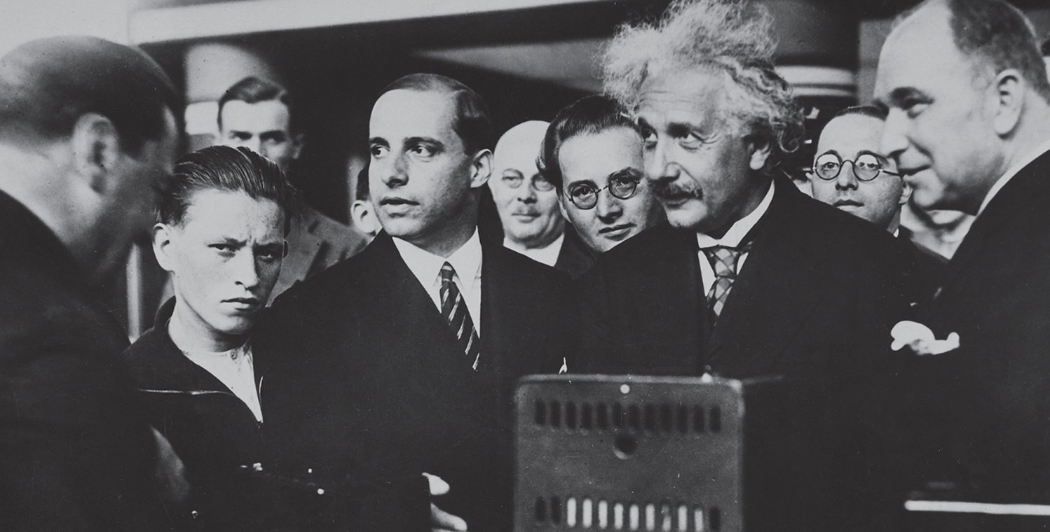 photograph from 1930 of eleven men, one of whom is Albert Einstein, gathered around a radio